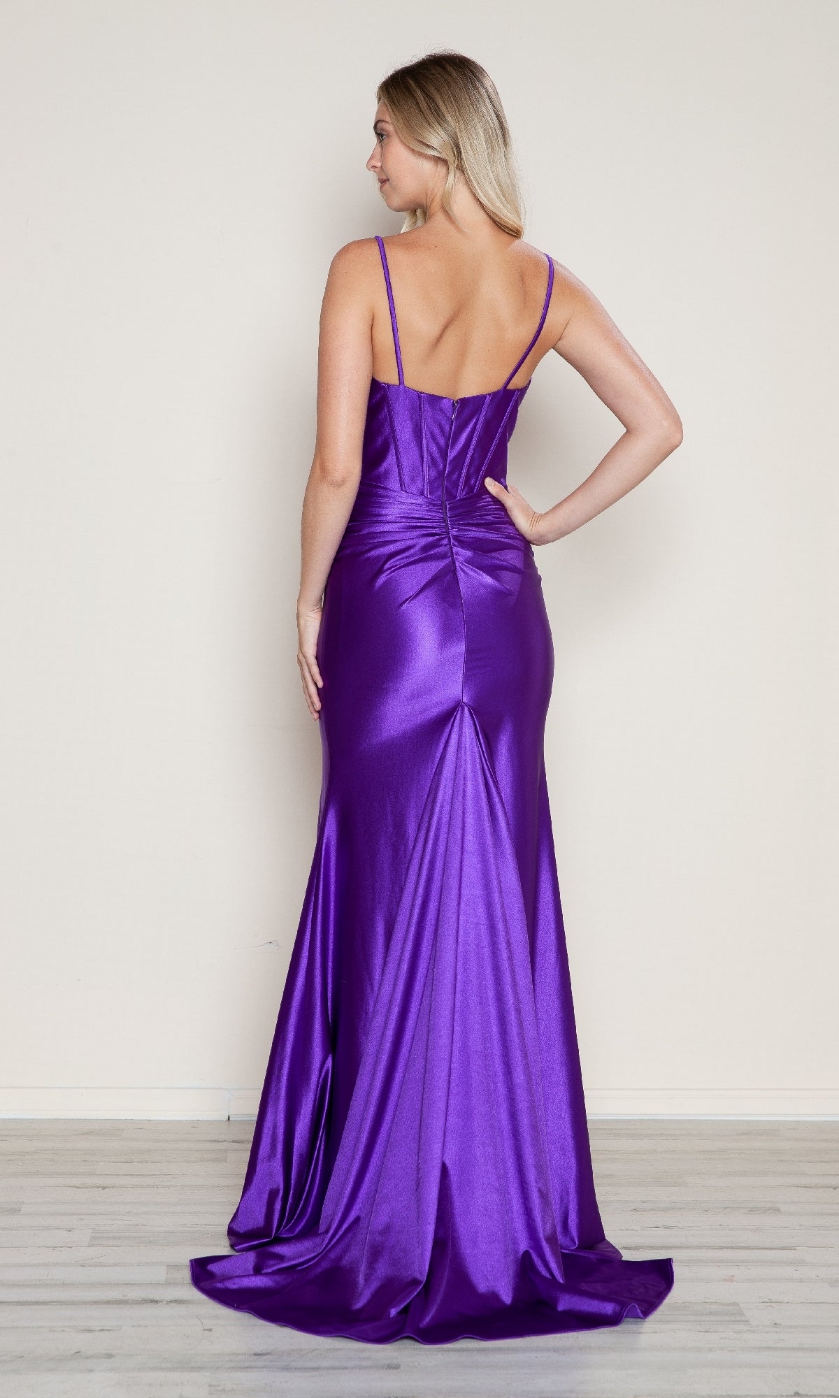 A woman faces away, wearing the Front-Bow Long Cut-Out Prom Dress (Poly USA 9644)—a floor-length, fitted purple gown with thin straps and a slight train—set against a plain light background.